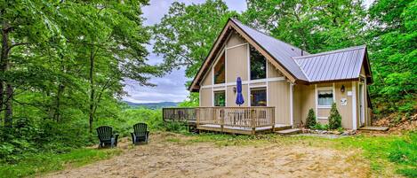 A cabin with a porch, surrounded by trees and a dirt path.