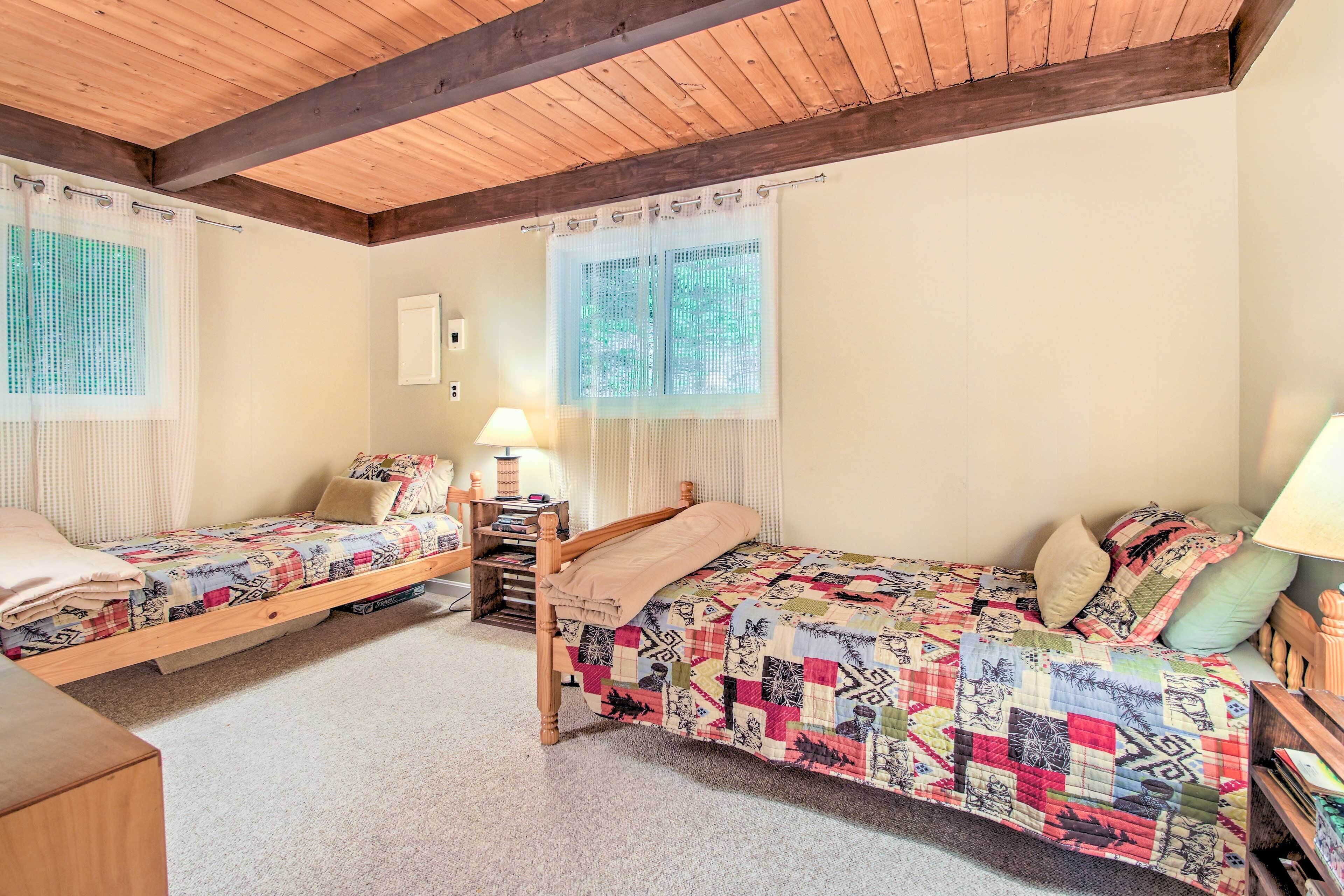Camera da letto con due letti singoli, poggiatesta in legno, soffitto in legno e una finestra con vista sugli alberi.