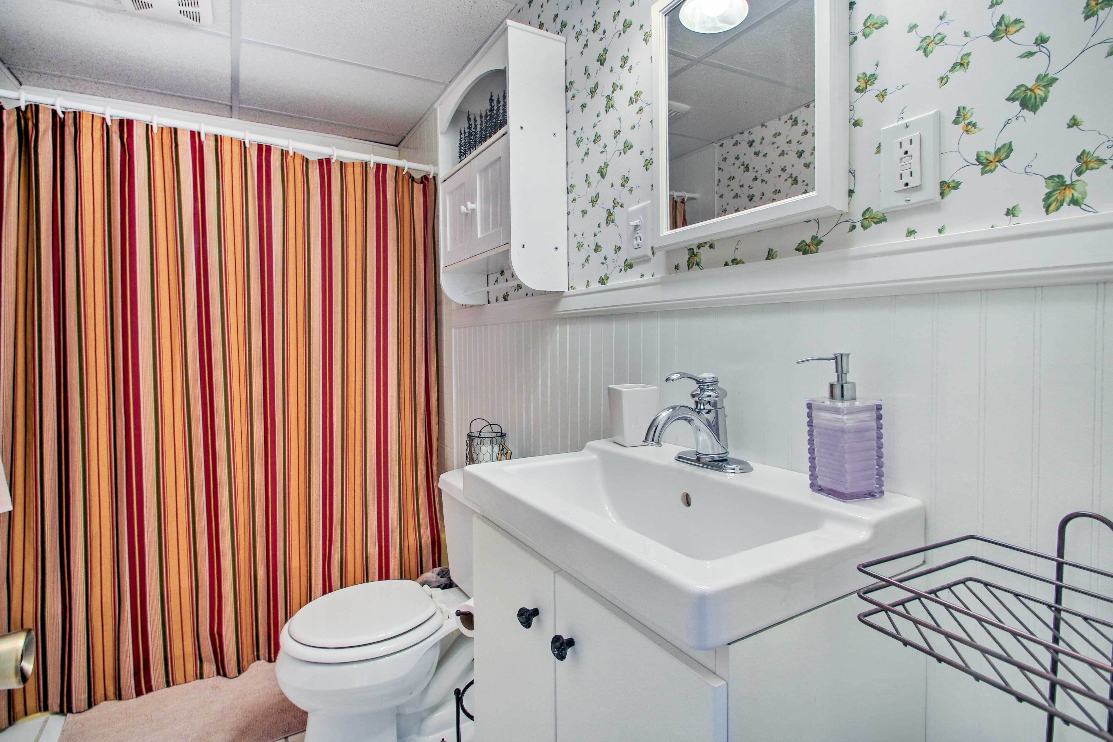 A bathroom with a striped curtain, a white sink with a soap dispenser, and a mirror above the sink.