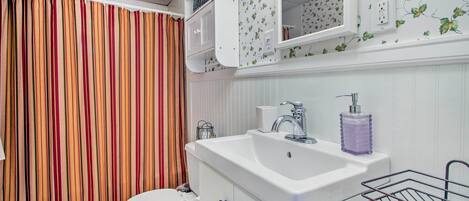 A bathroom with a striped curtain, a white sink with a soap dispenser, and a mirror above the sink.