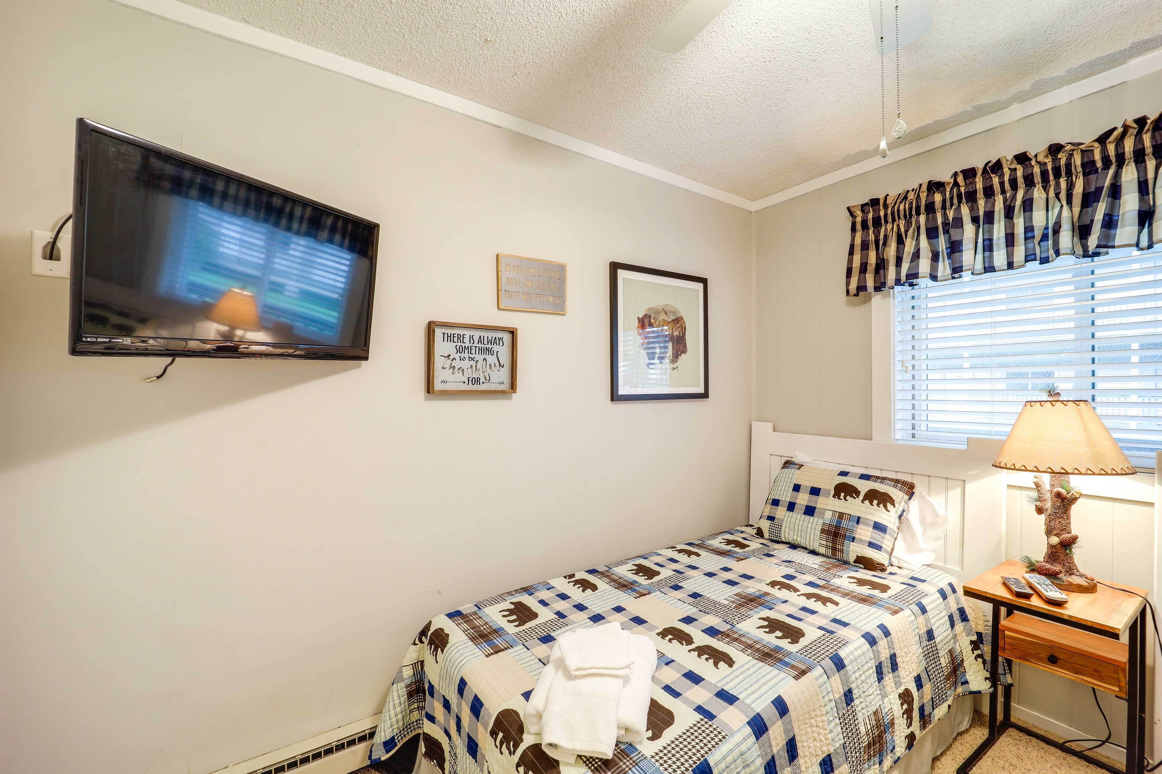 A bedroom with a bed, a TV mounted on the wall, a bedside table with a lamp, and a window with blinds.