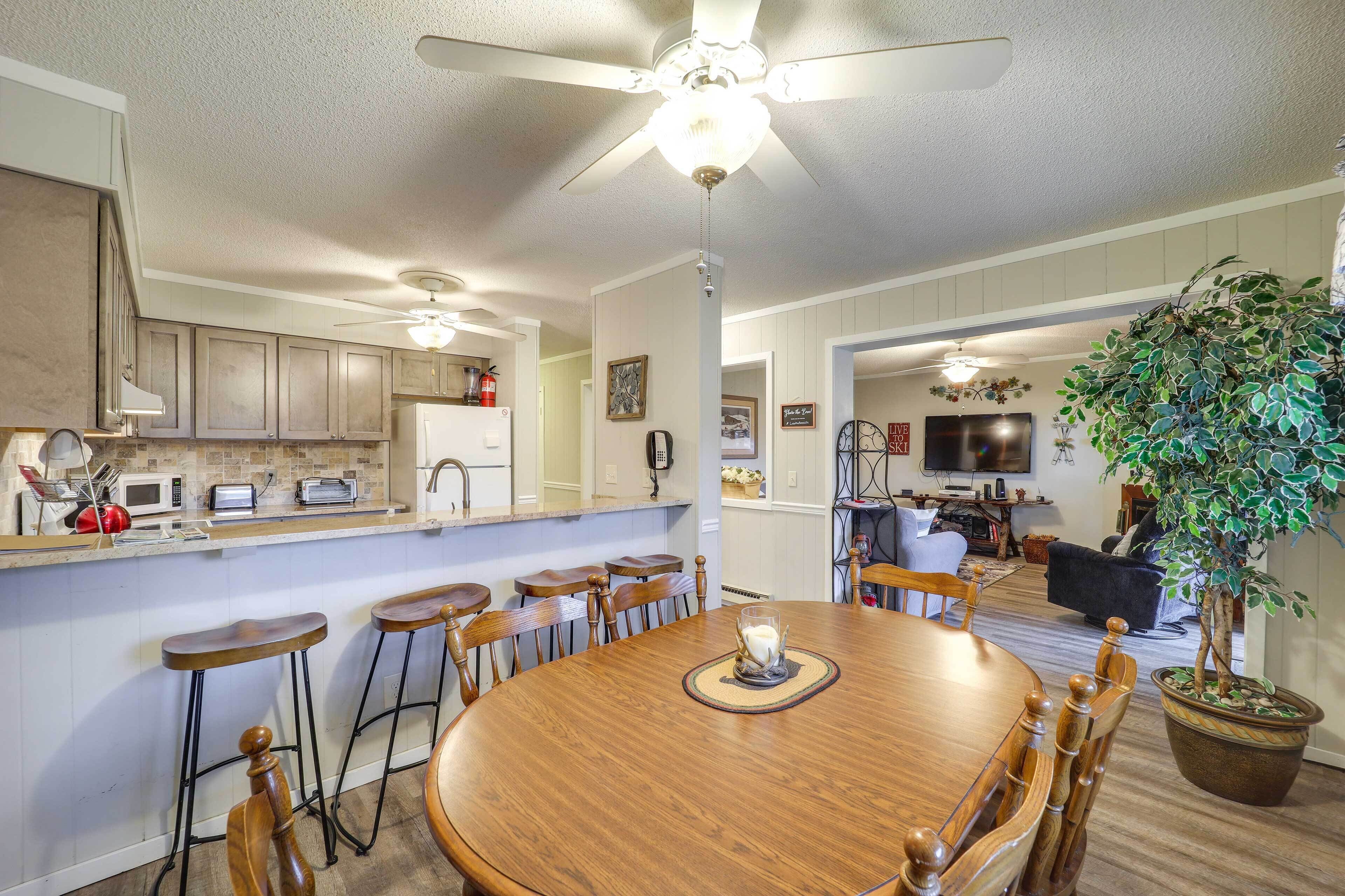 A dining area with a wooden table, bar stools, and a ceiling fan.