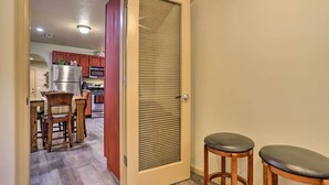 Un couloir mène à une cuisine équipée de meubles en bois, d’un réfrigérateur en acier inoxydable et d’une porte-fenêtre coulissante.