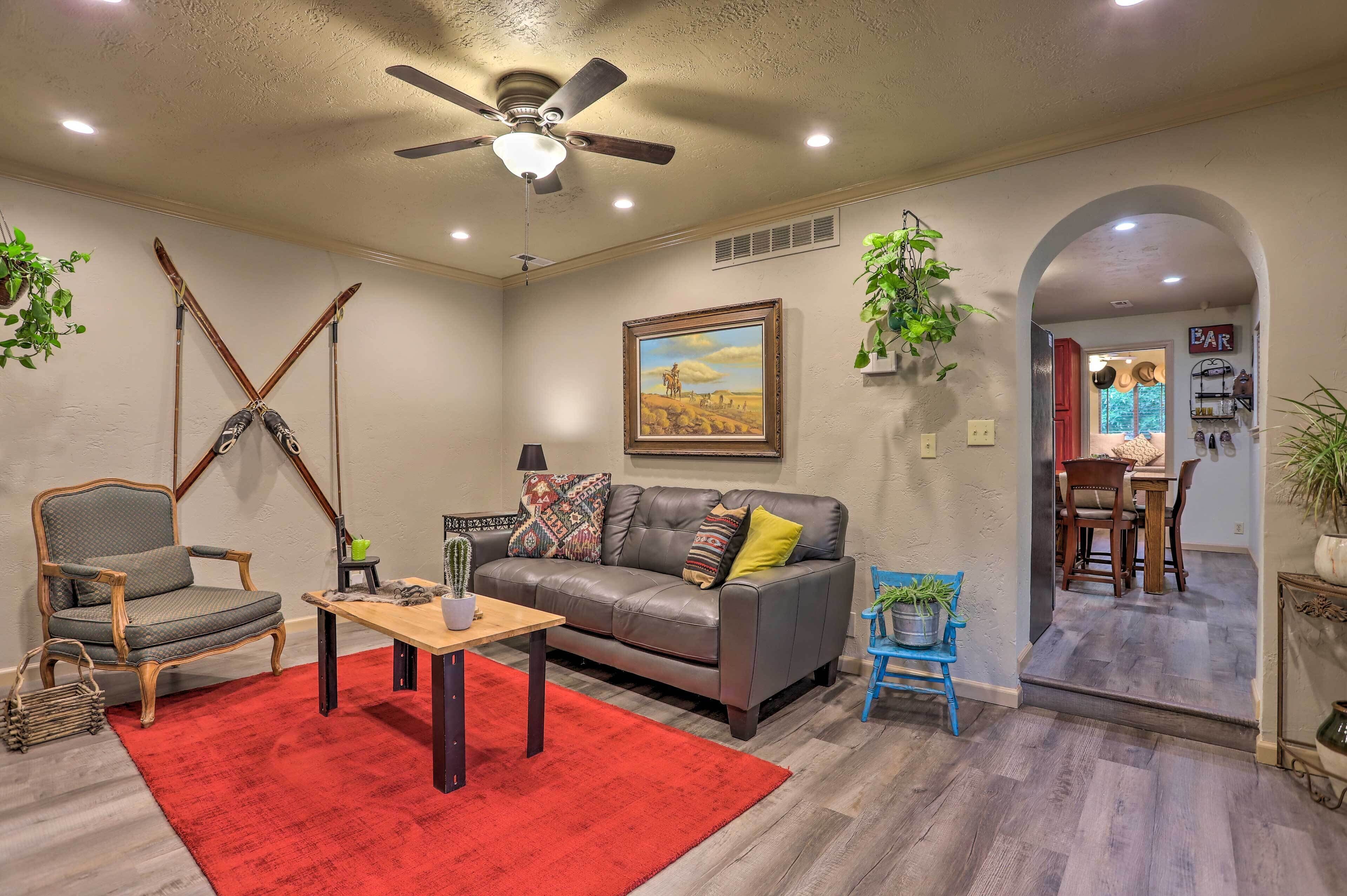 A living room with a sofa, armchair, and coffee table, a ceiling fan, and a painting on the wall.