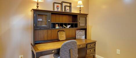 A wooden desk with a chair, lamps, and shelves.