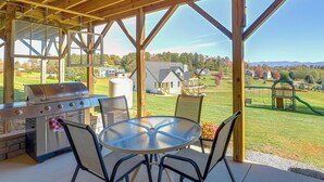 Une terrasse extérieure équipée d’un barbecue, de chaises et d’une table, donnant sur un quartier résidentiel avec des maisons et une aire de jeux.