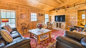 A log cabin interior with a wooden ceiling, leather sofas, a wooden coffee table, a television, and a fireplace. - Cozy New Braunfels Family Cabin w/ Porch & Views! (New Braunfels)