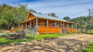 A wooden cabin with a porch, surrounded by a stone wall and a gravel path. - Cozy New Braunfels Family Cabin w/ Porch & Views! (New Braunfels)