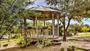 A wooden gazebo with a roof and lanterns, surrounded by greenery and potted plants. - Cozy New Braunfels Family Cabin w/ Porch & Views! (New Braunfels)