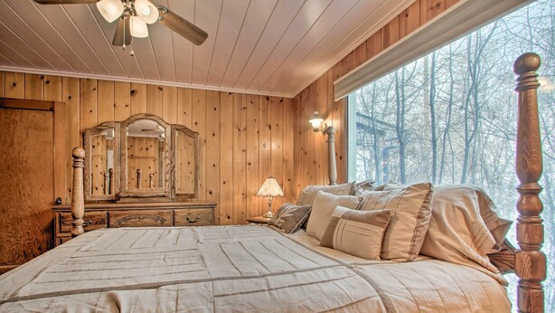 A bedroom with a large bed, wooden walls, a ceiling fan, a mirror, and a window with a view of trees. - Cozy Home w/ Hot Tub: Half Mi to Salmon River! (Salmon)