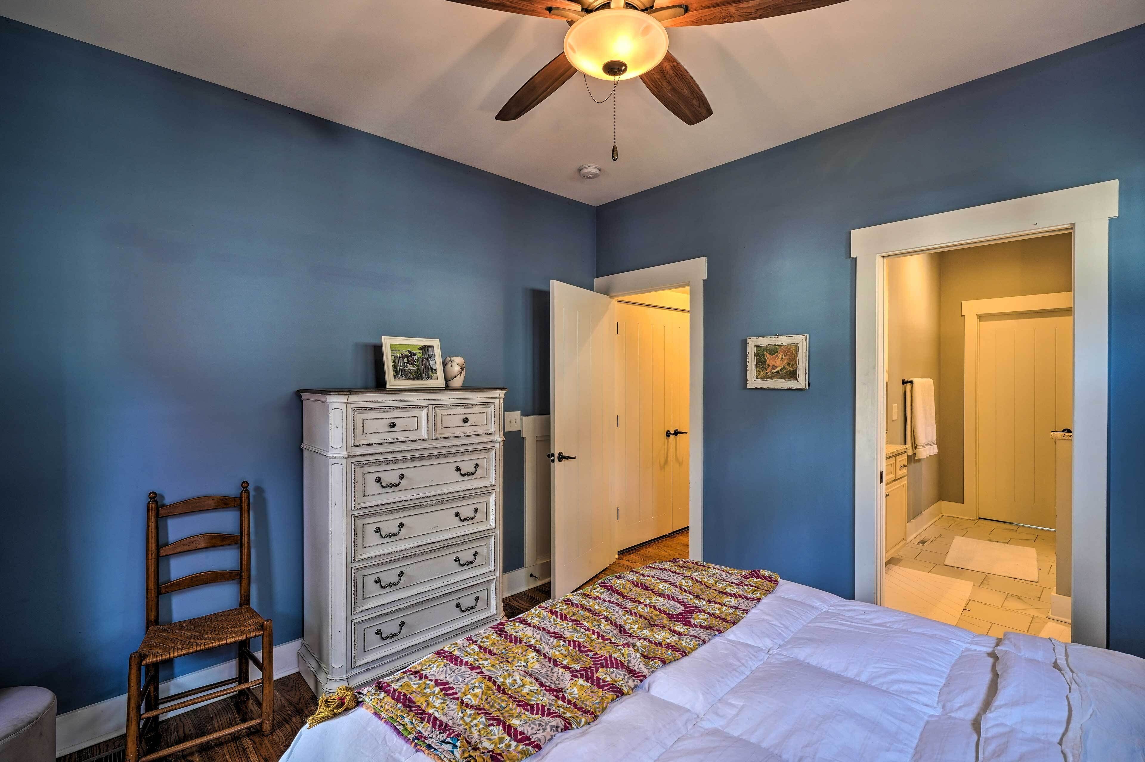 A bedroom with a bed, a dresser, a chair, and a door leading to a bathroom.