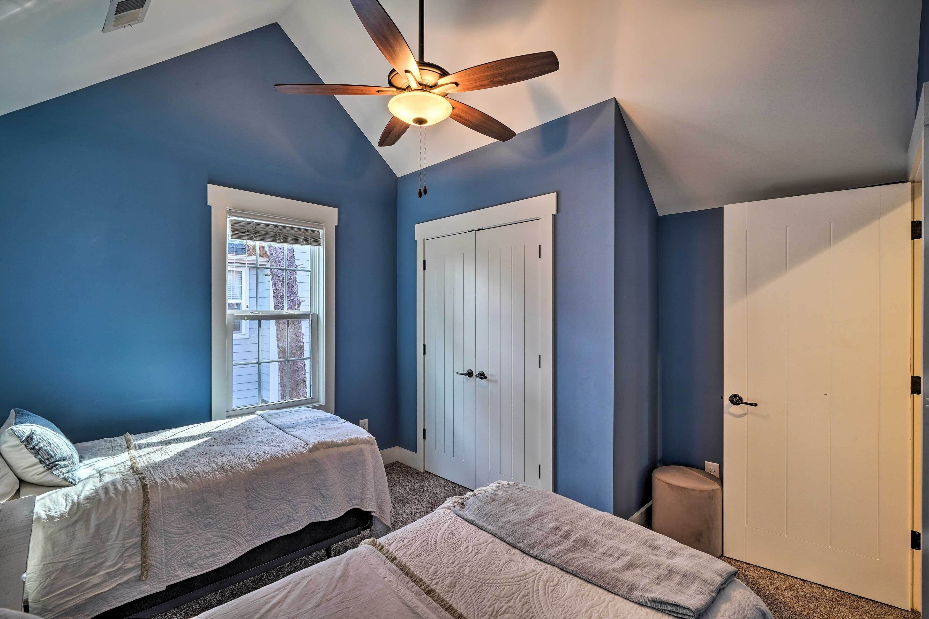 A bedroom with two beds, a ceiling fan, a window, and a door.