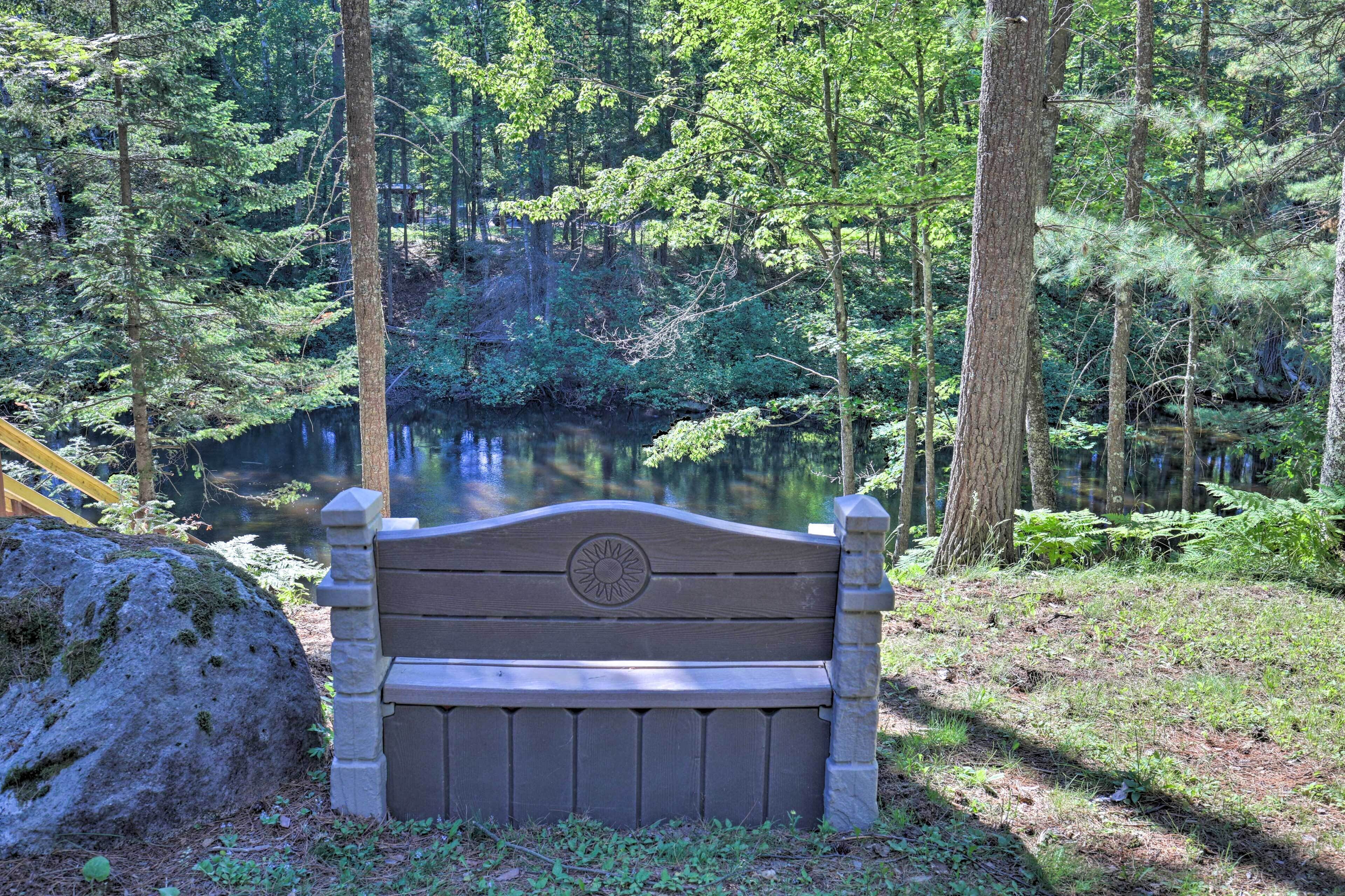 A wooden bench with a sun emblem, surrounded by a forest and a body of water.