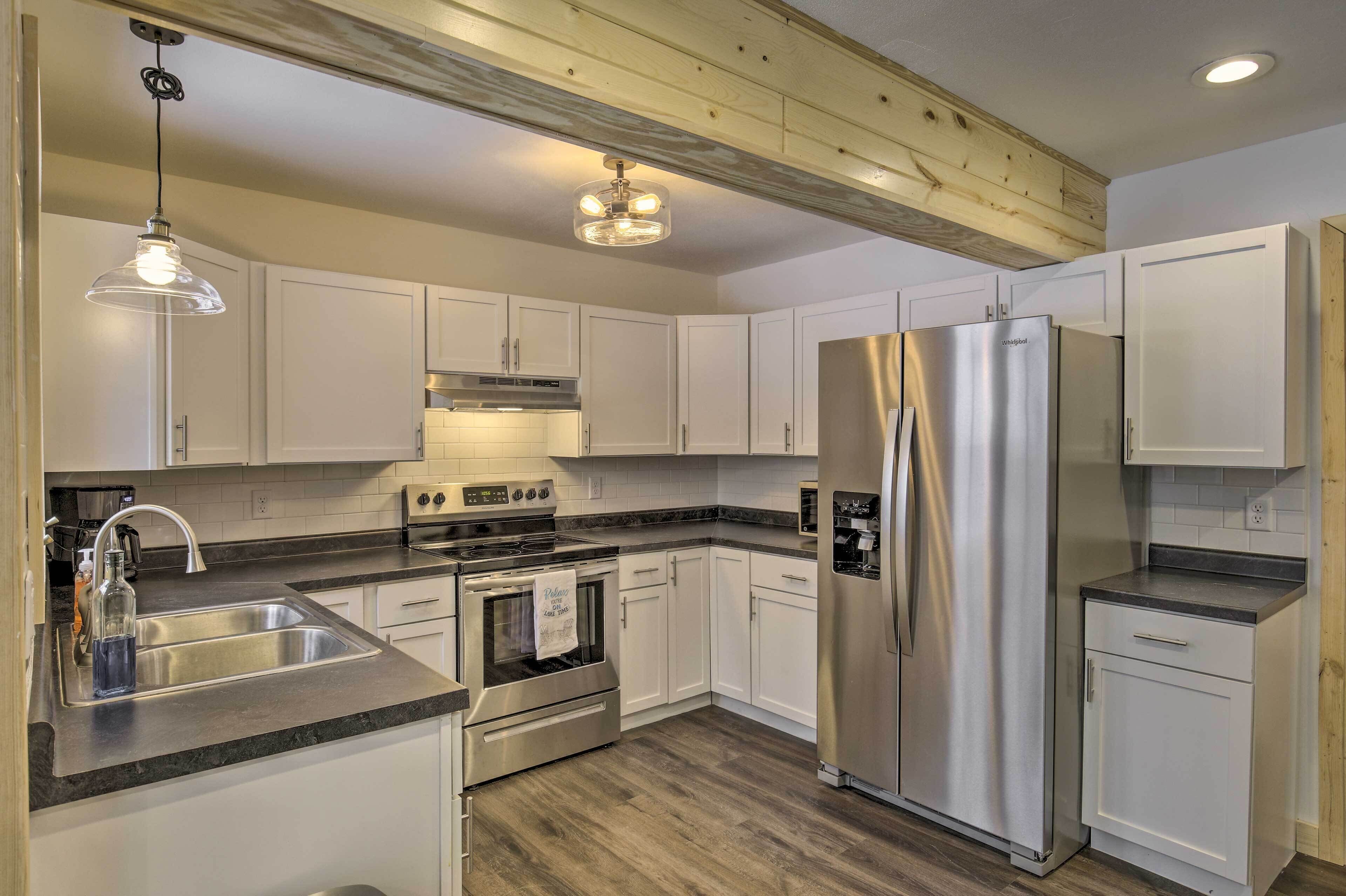 A modern kitchen with white cabinets, stainless steel appliances, a granite countertop, and a wooden ceiling beam.