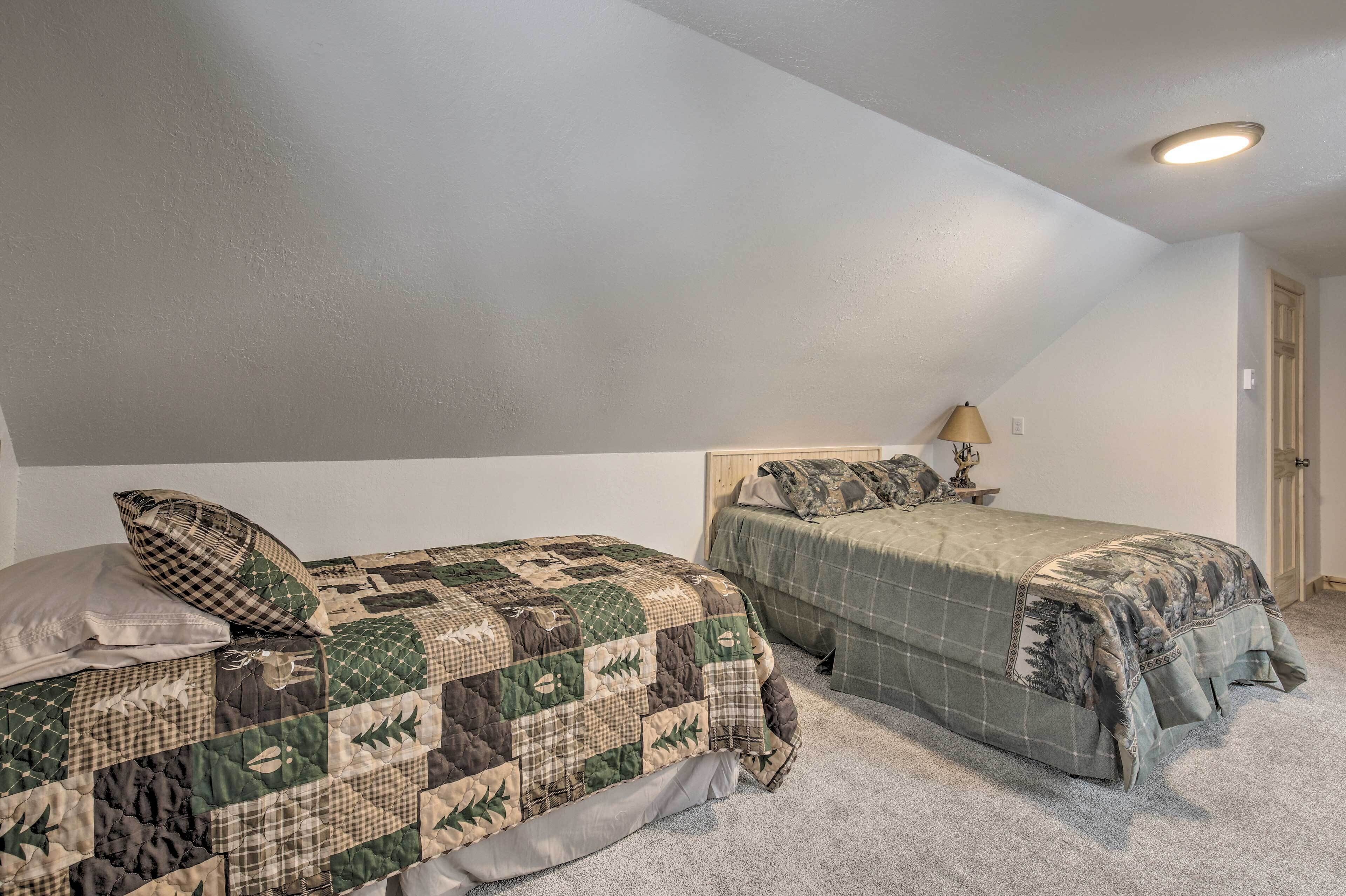 Two twin beds with patterned quilts, a ceiling light, and a door in a room with carpeted flooring.