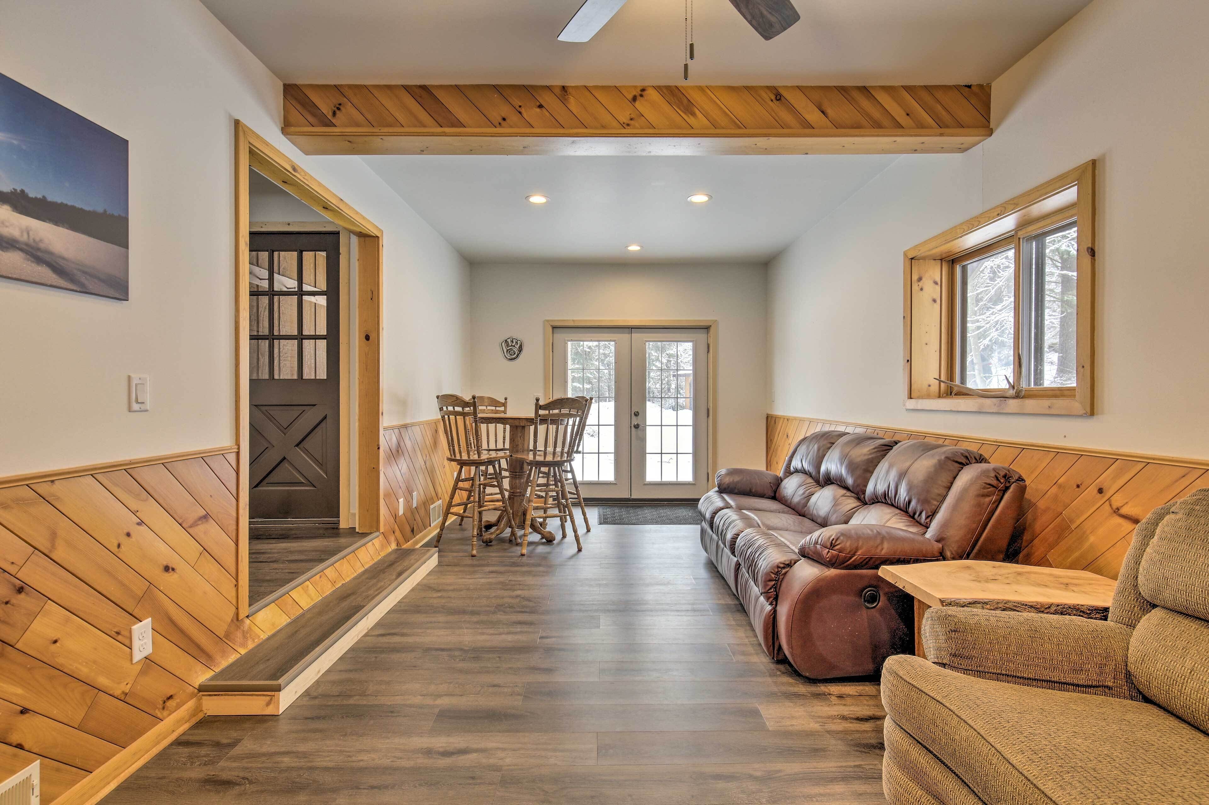 A spacious room with a wooden floor, a brown leather sofa, a dining table with chairs, and a large window.