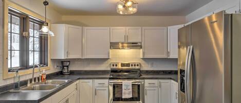 A modern kitchen with white cabinets, stainless steel appliances, and a wooden ceiling.