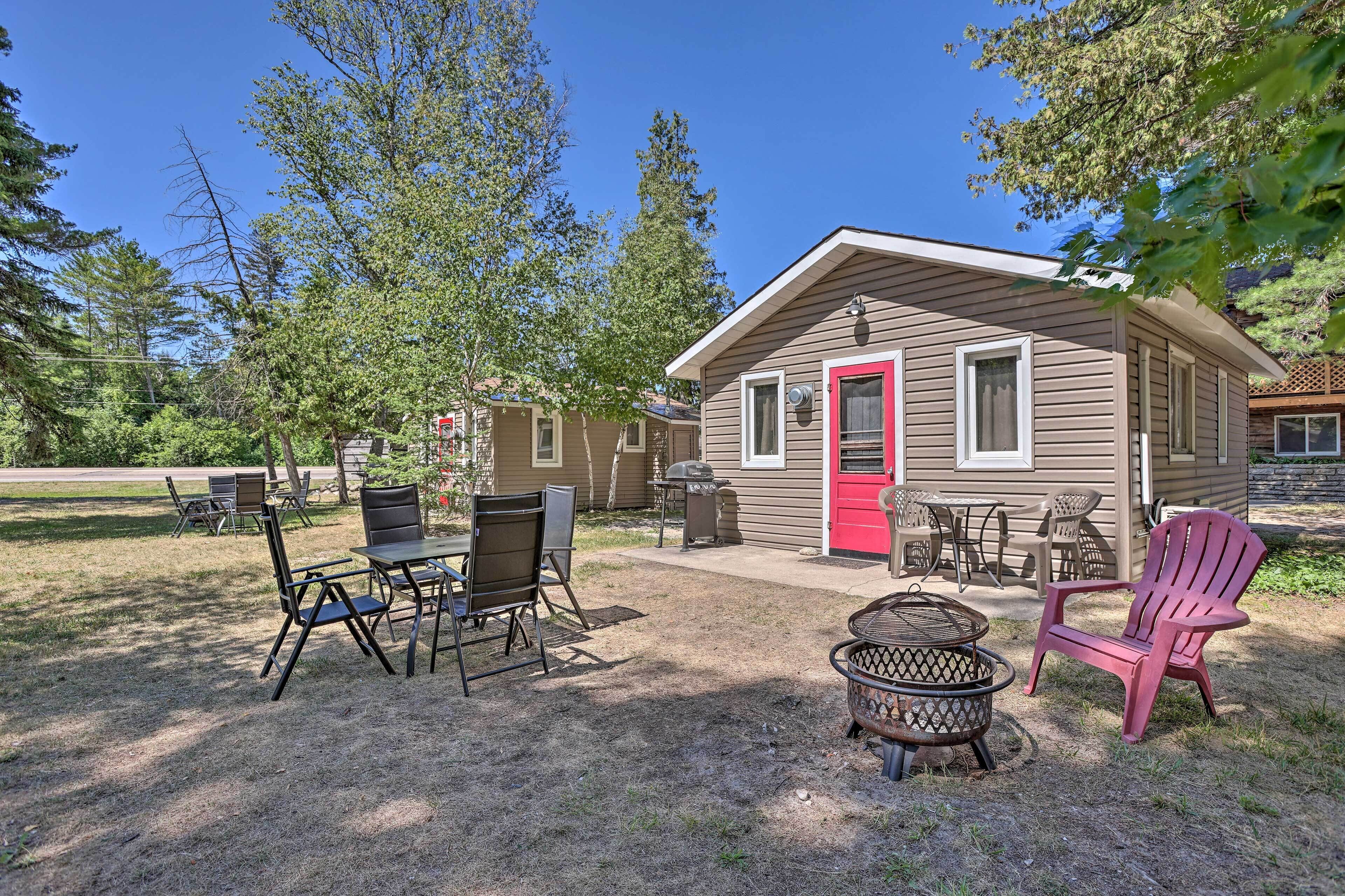 A small cabin with a red door, outdoor seating, and a fire pit.