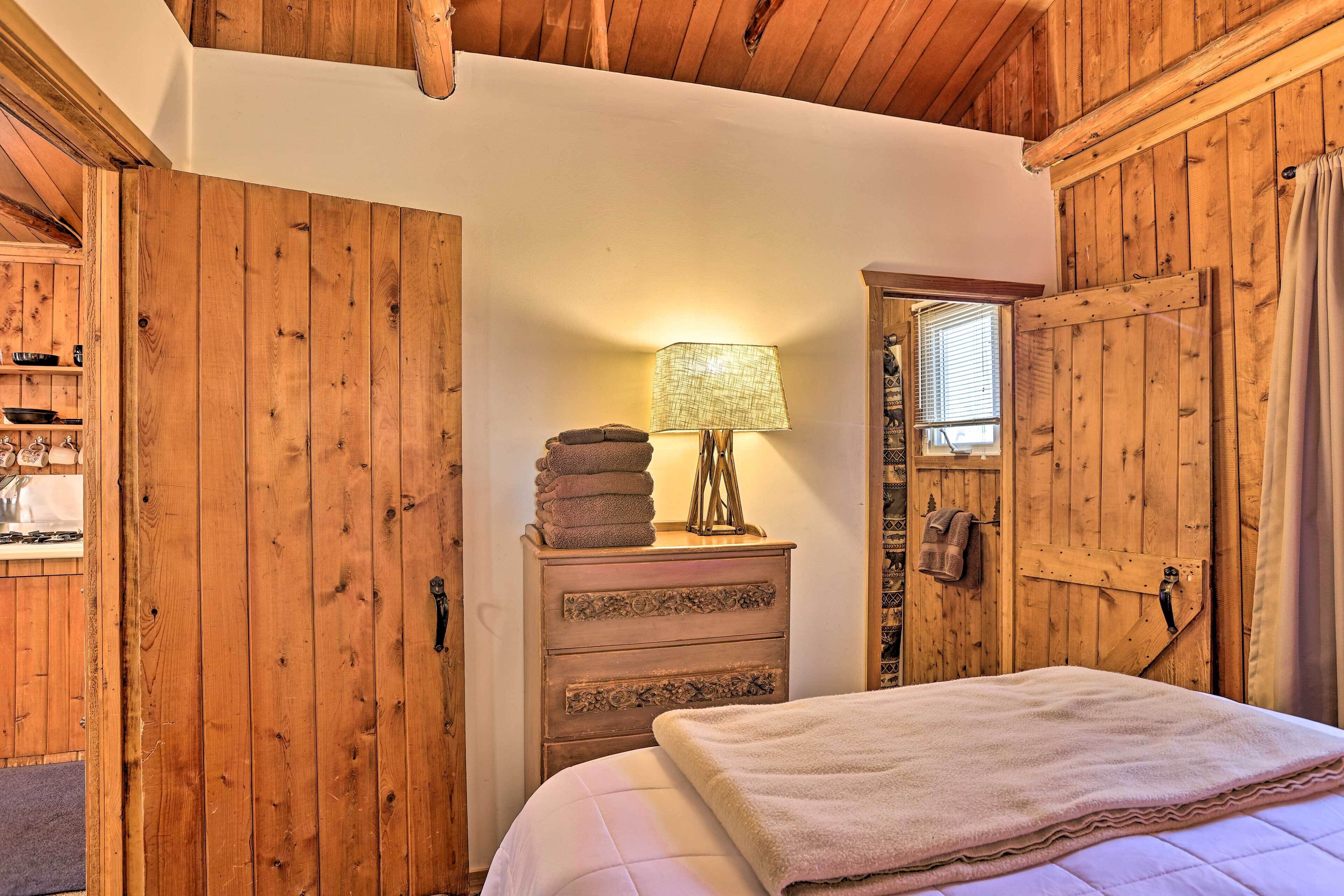 Une pièce en bois avec un lit, une commode surmontée d’une lampe et une porte.