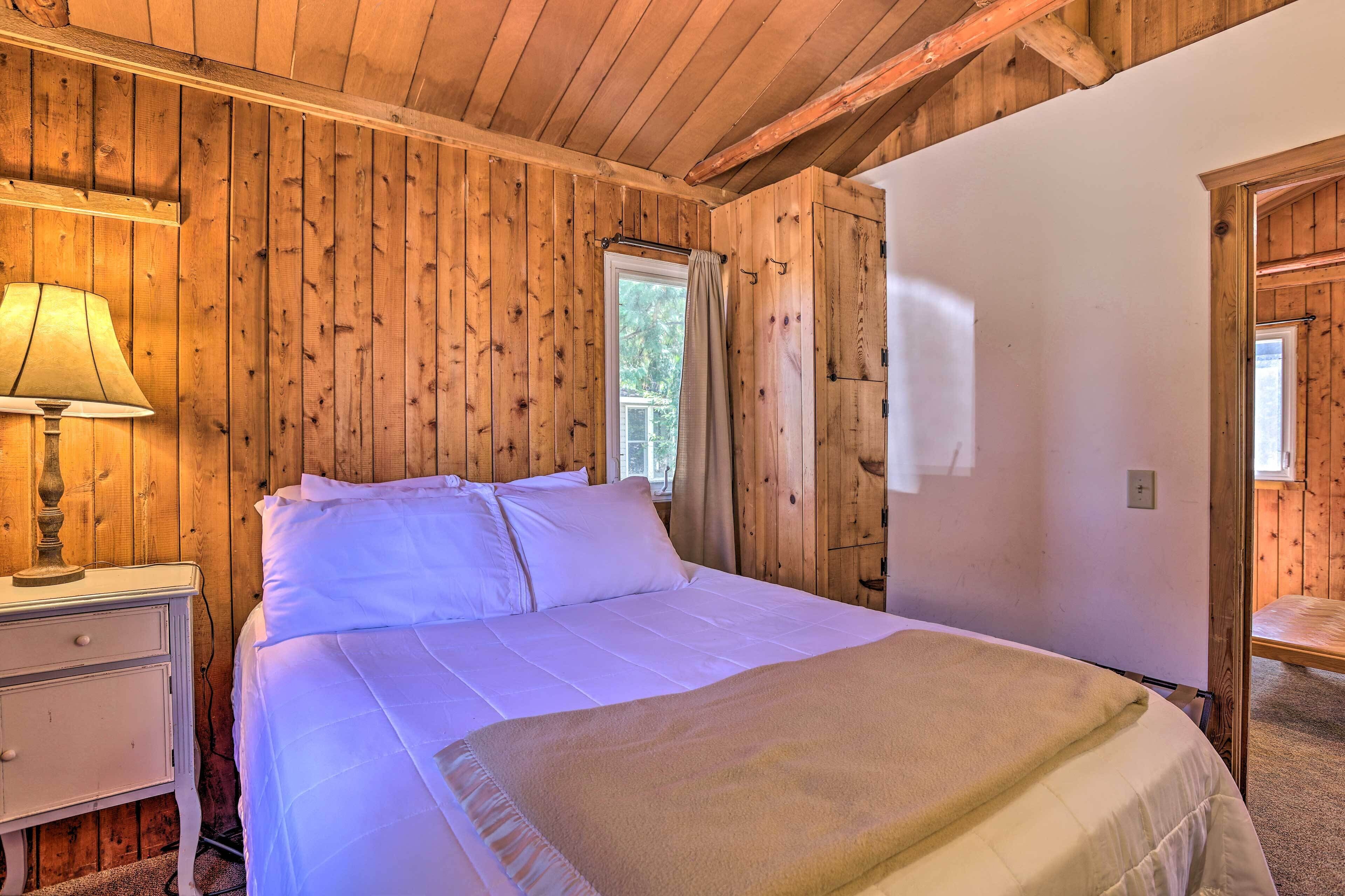 Quarto com painéis de madeira, uma cama, uma mesa de cabeceira e uma janela.