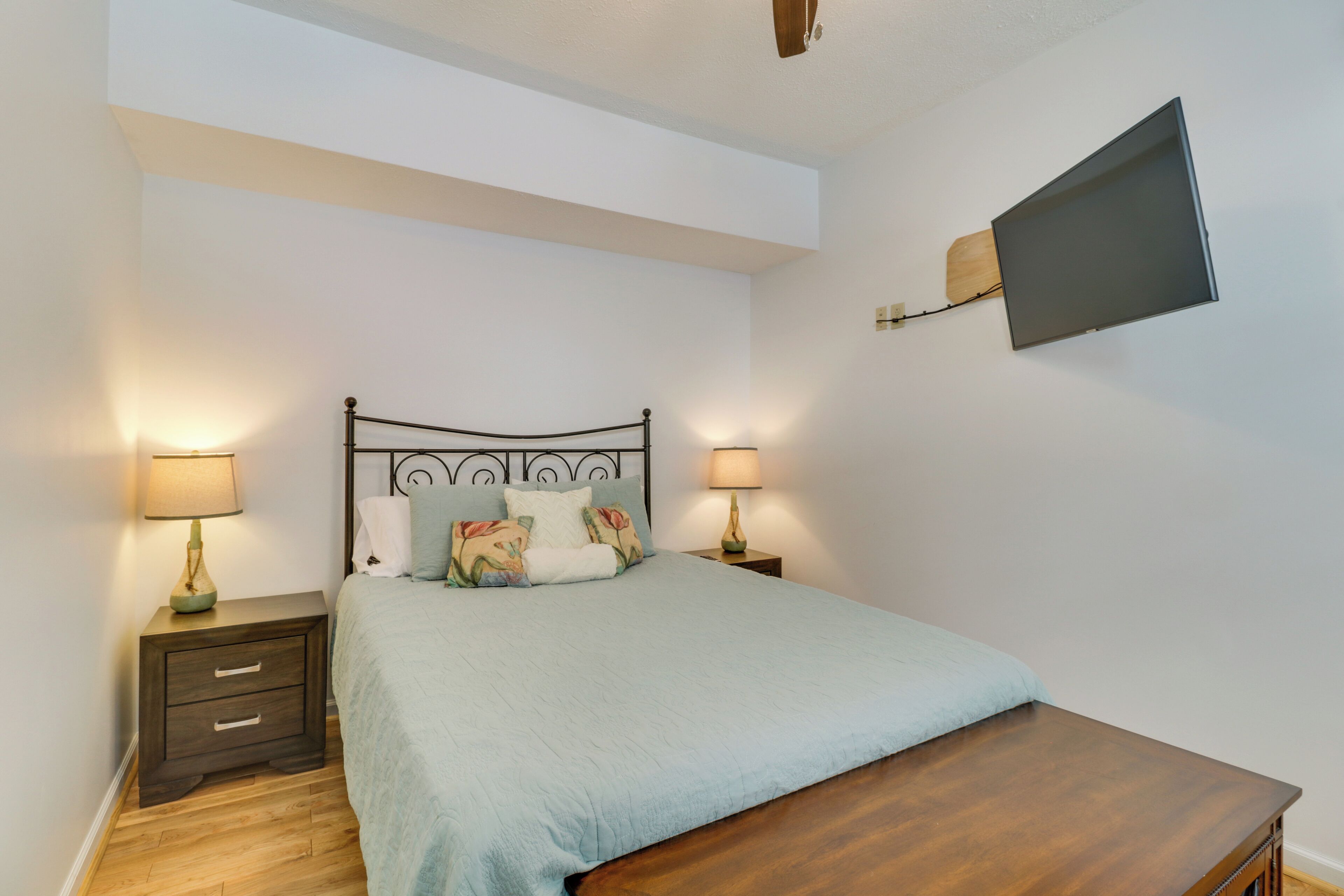 A bedroom with a bed, two bedside tables, a flat-screen TV mounted on the wall, and a wooden nightstand.