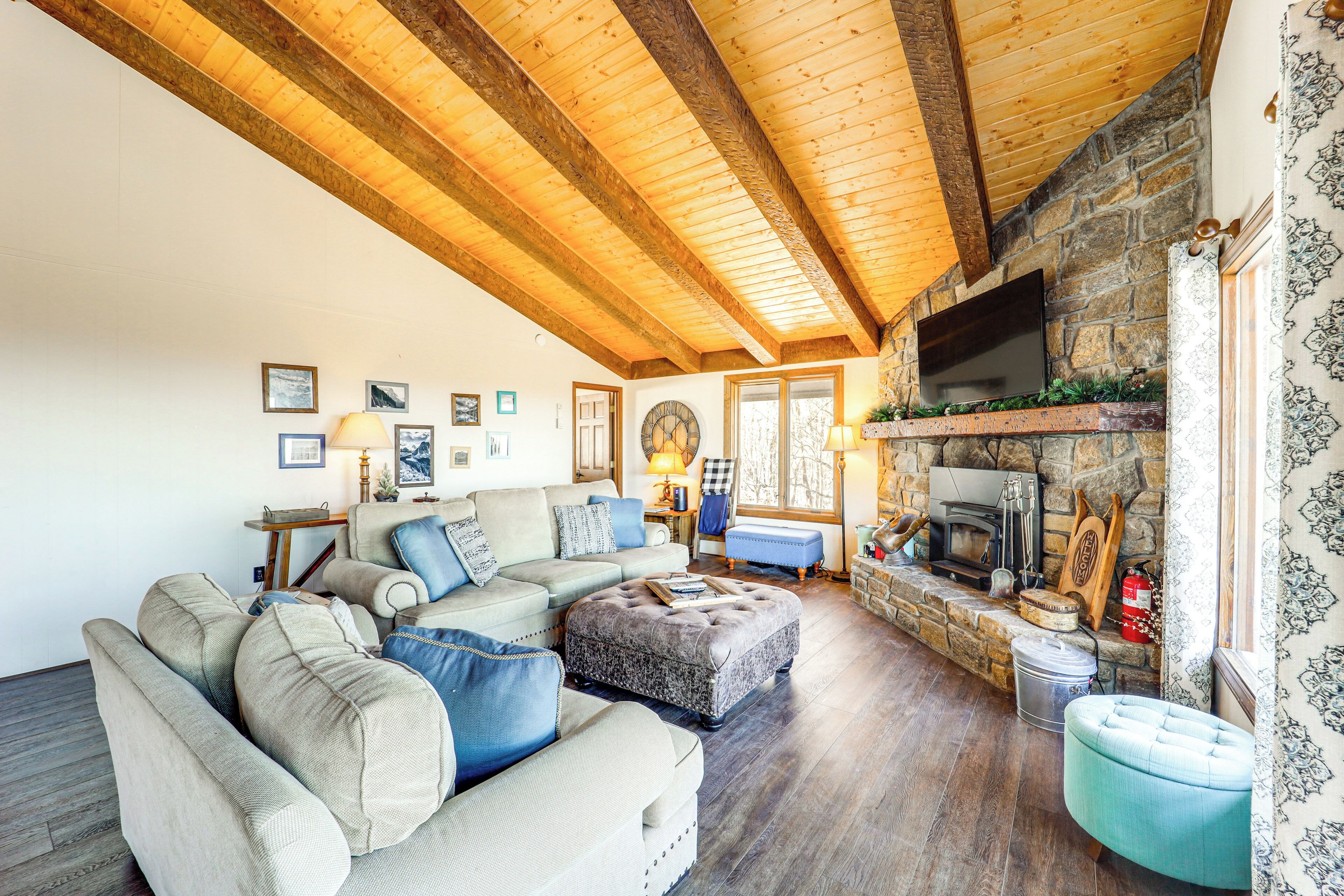 Ein gemütliches Wohnzimmer mit Kamin aus Stein, Holzbalken und einem großen Fernseher.