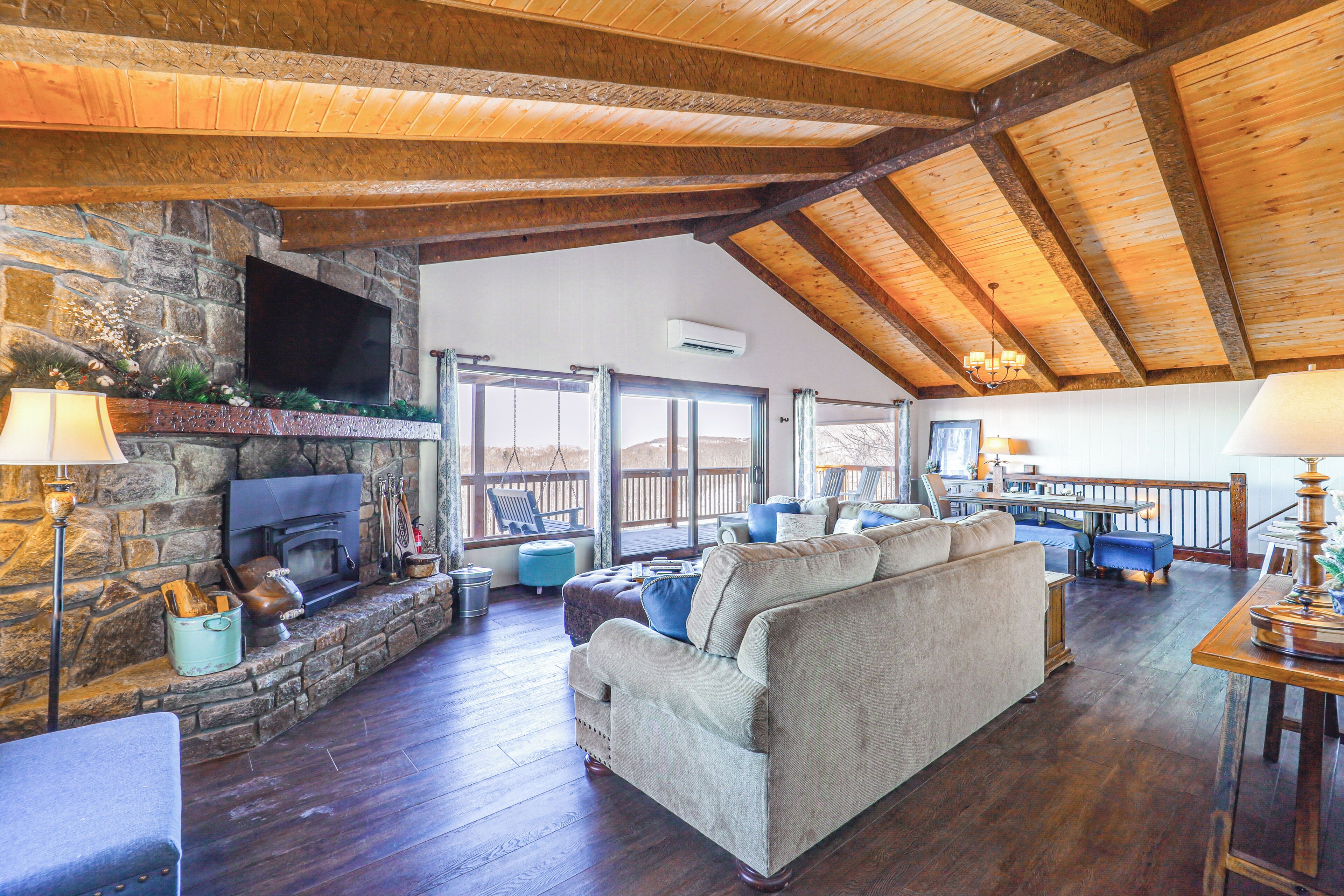 A spacious living room with a stone fireplace, wooden beams, and a large couch.
