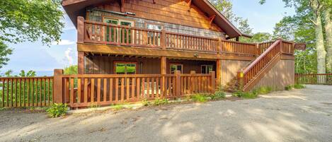 A two-story wooden cabin with a balcony, a covered porch, and a staircase leading to the upper level.