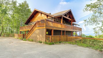 A two-story wooden cabin with a balcony and a staircase leading to the upper level.