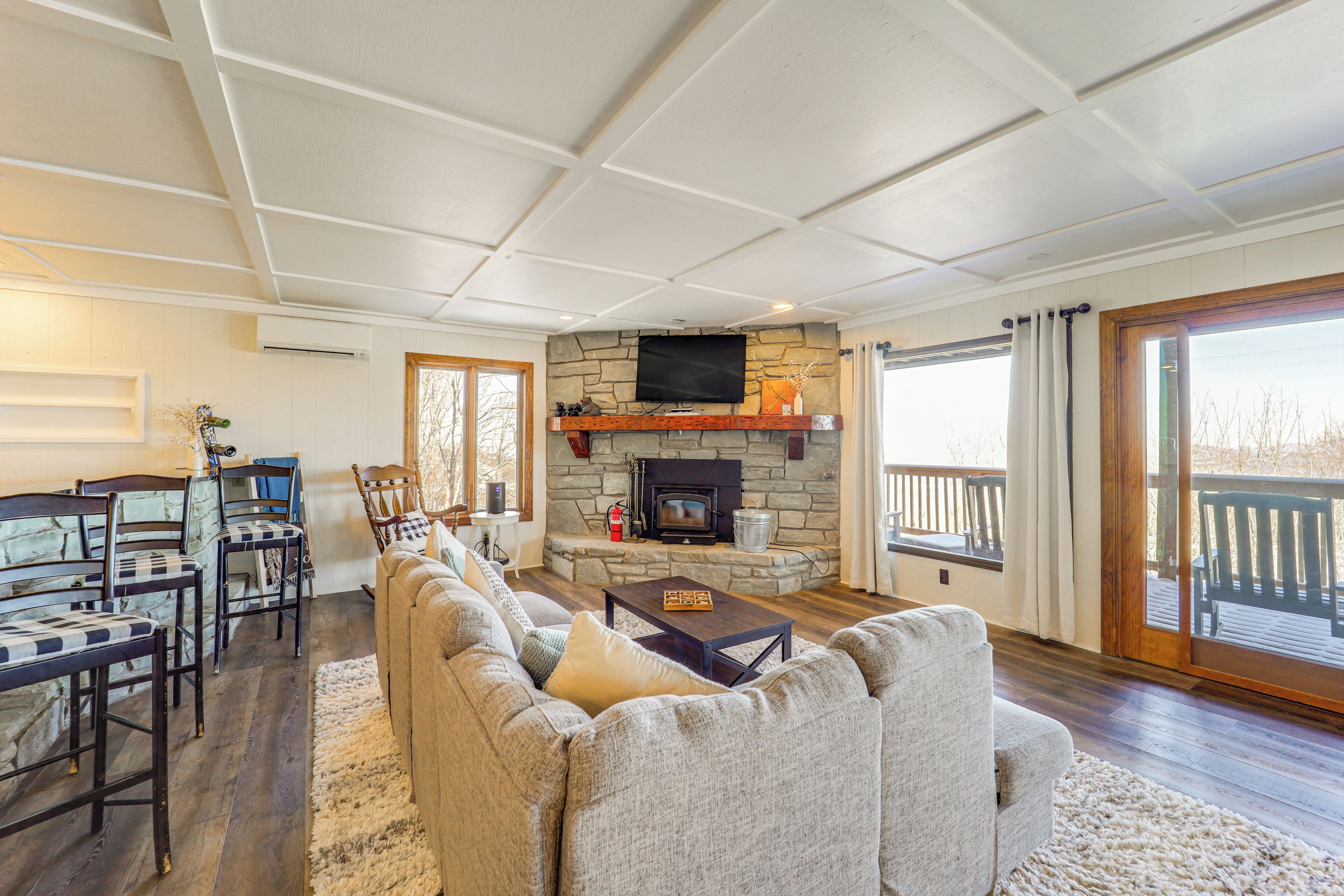 A spacious living room with a stone fireplace, a large sofa, and a television mounted on the wall.