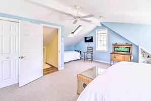 A bedroom with a sloped ceiling, a ceiling fan, a bed, a dresser, and a television on the wall.