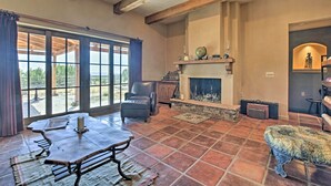 A spacious living room with a fireplace, large windows, and a stone fireplace surround. - Charming Mountain Estate w/ Views + Fire Pit! (Cerrillos)