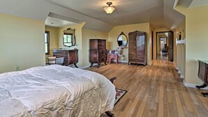 A spacious bedroom with a large bed, wooden flooring, and a hallway leading to other rooms. - Charming Mountain Estate w/ Views + Fire Pit! (Cerrillos)