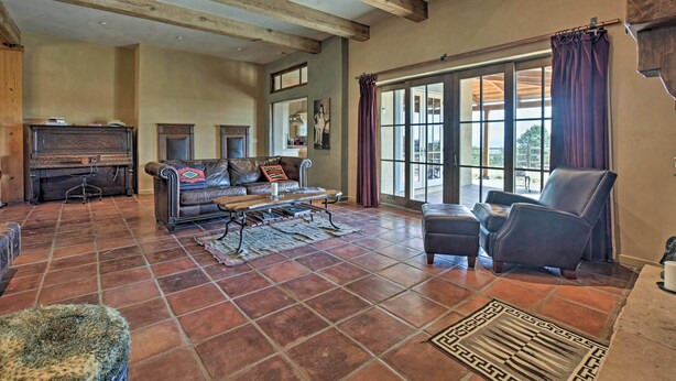 A spacious living room with a fireplace, leather furniture, and large windows. - Charming Mountain Estate w/ Views + Fire Pit! (Cerrillos)