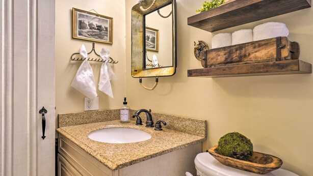 A bathroom with a granite countertop sink, a mirror, a towel rack, a toilet, and a shelf with towels. - Dreamy Homestead Escape: Patio, Ranch On-site (Crossville)