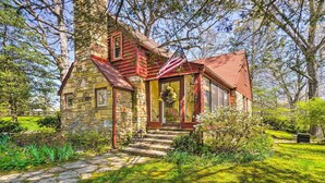 A stone house with a red roof and a porch, surrounded by lush greenery and trees. - Dreamy Homestead Escape: Patio, Ranch On-site (Crossville)