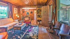 Una habitación acogedora con paredes y techo de madera, un sofá, una silla, una mesita y una ventana con cortinas.