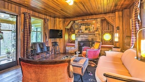 Un acogedor interior de cabaña con techo de madera, chimenea, televisor y asientos cómodos.