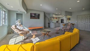A spacious living area with a yellow sofa, a round coffee table, and a reclining chair. There is a bench along the wall and a kitchen area in the background. - Falling Water Chalet Upper Unit: Near Bike Trails! (Bella Vista)