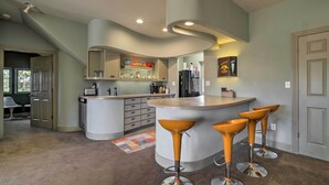 A modern kitchen with a curved island, bar stools, and a refrigerator. - Falling Water Chalet Upper Unit: Near Bike Trails! (Bella Vista)
