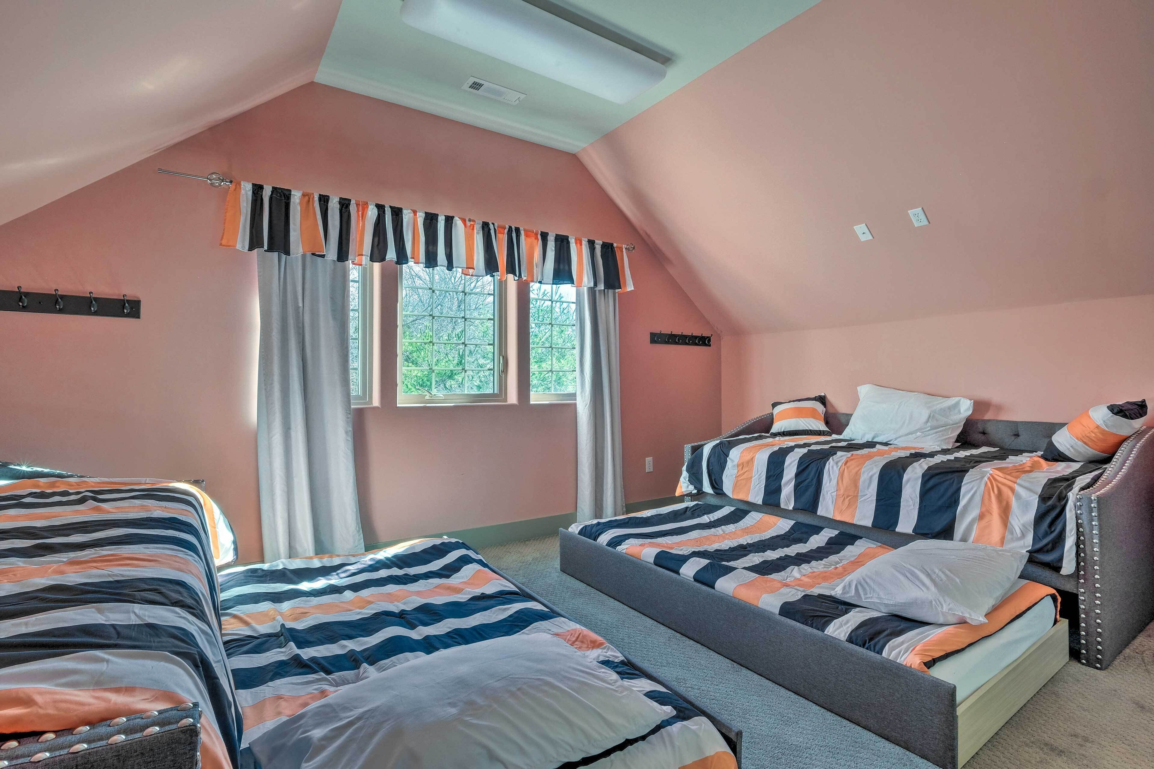 A bedroom with two beds, a sloped ceiling, and a window with curtains.