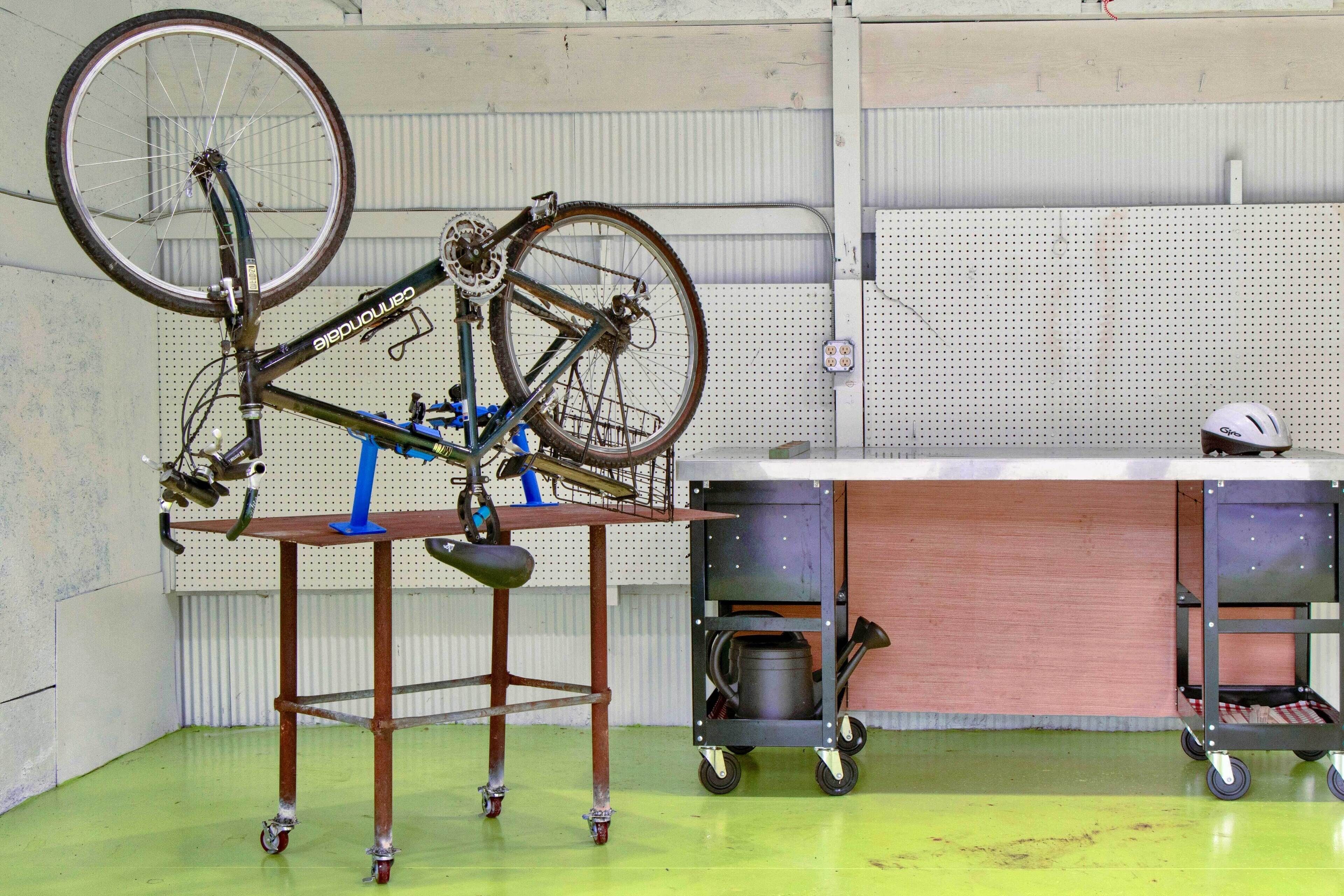 A bicycle mounted on a stand in a workshop with a workbench and storage cabinets.