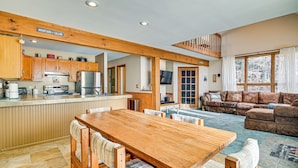 Ein großzügiger Wohnbereich mit Esstisch und Stühlen aus Holz, einem gemütlichen Sofa und einer Küche mit Holzschränken und einem großen Fenster.