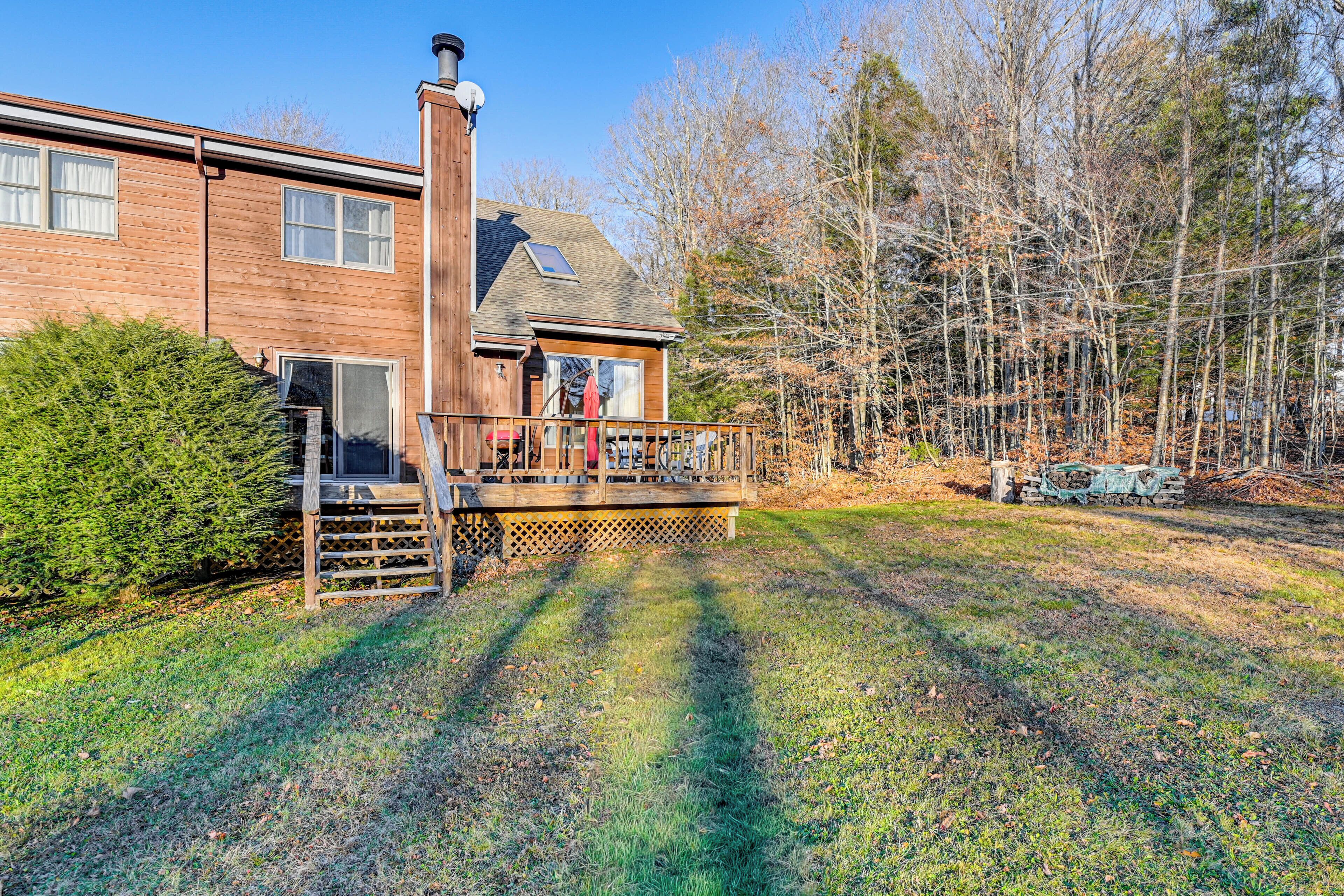A two-story wooden house with a deck, surrounded by trees and a grassy yard.