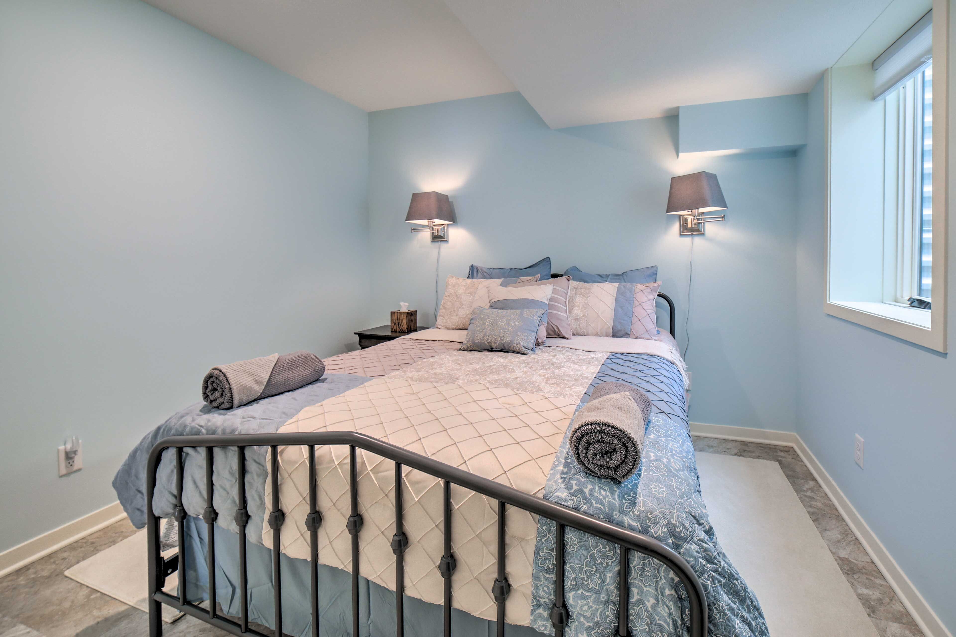 A bedroom with a bed, two wall-mounted lamps, a nightstand, and a window.