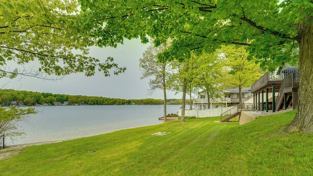 Una propiedad junto al lago con césped, una terraza de madera y una casa con balcón con vistas al agua.