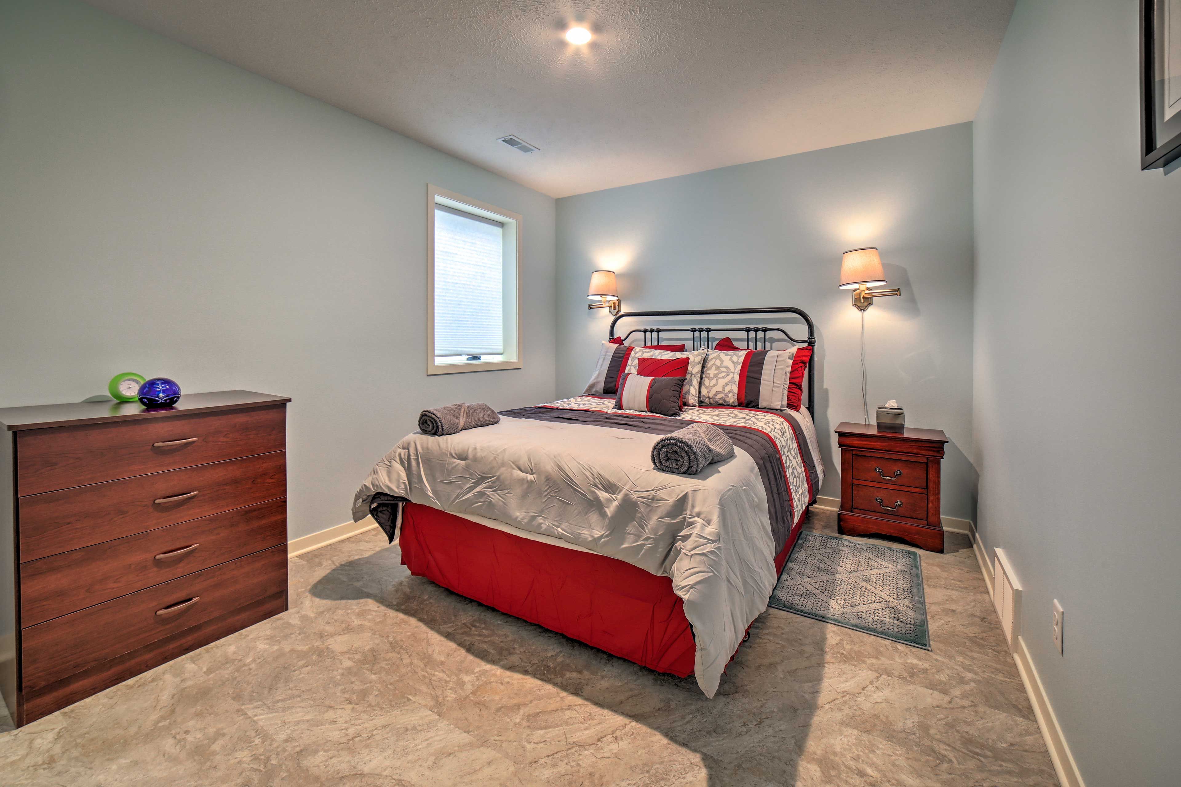 A bedroom with a bed, dresser, nightstand, lamp, and a window.