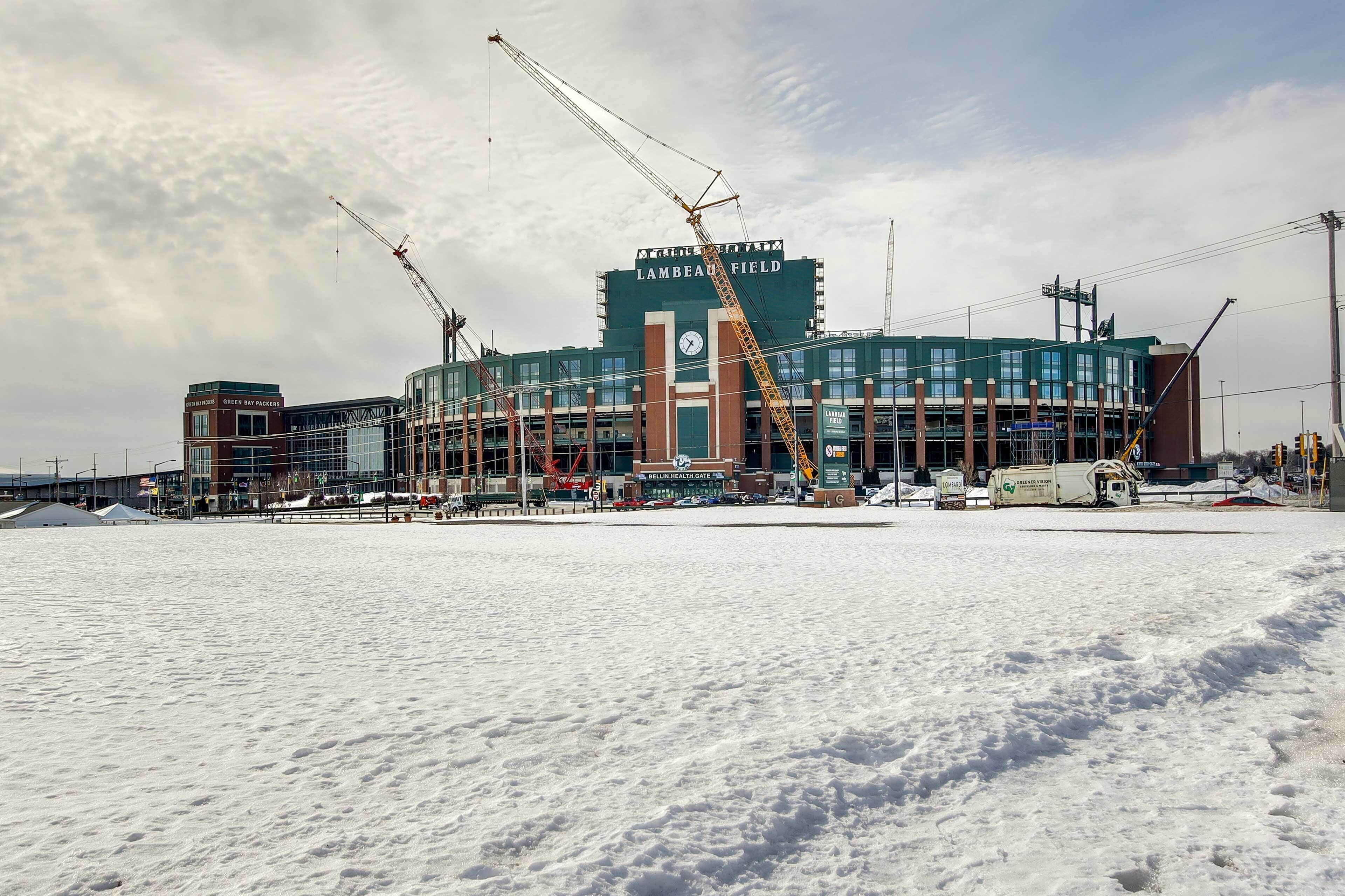 Un estadio con un gran letrero verde, varias grúas y terreno cubierto de nieve.