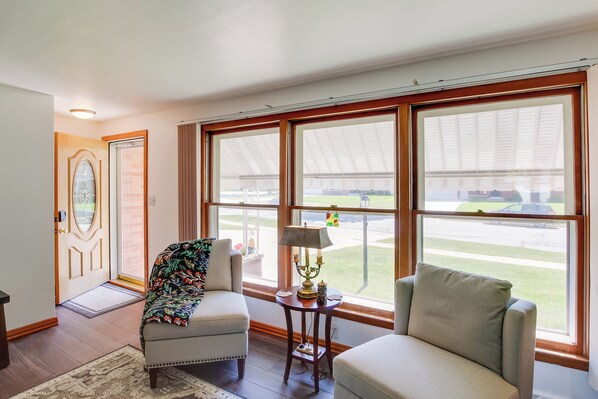 Una habitación amplia con ventanas grandes, una puerta con un panel de vidrio decorativo y dos sillones.