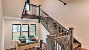 A modern staircase with dark wood railings and a beige cushioned bench by a large window. - Grand Long Branch Home: 1 Block to Beach! (Long Branch)